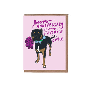 Pink background with image of black and brown dog holding a purple flower in its' mouth. Purple text says, " Happy anniversary to my favorite couple". Kraft envelope included. 