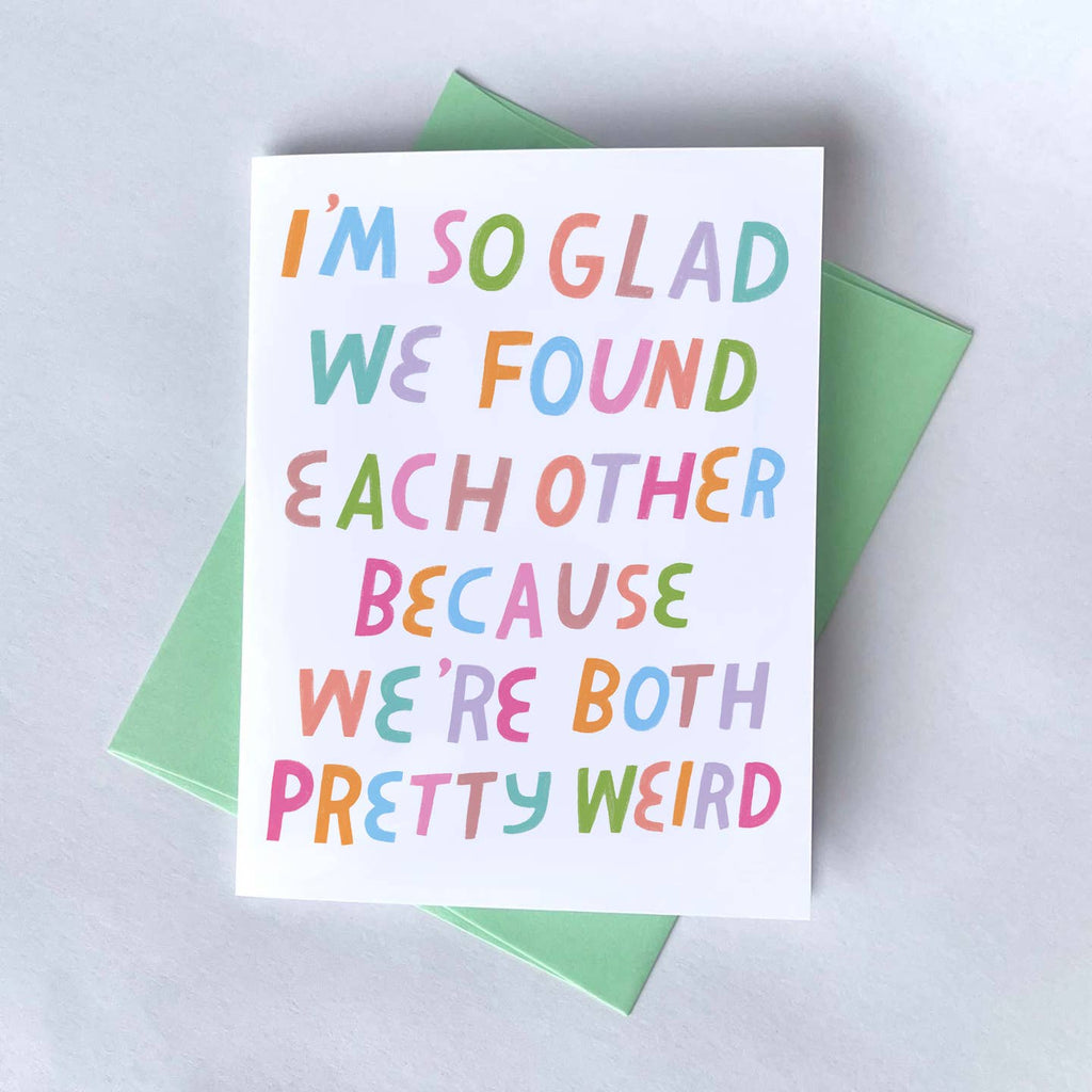 Greeting card with white background and multicolored text says, "I'm so glad we found each other becuase we're both pretty weird". Green envelope included.
