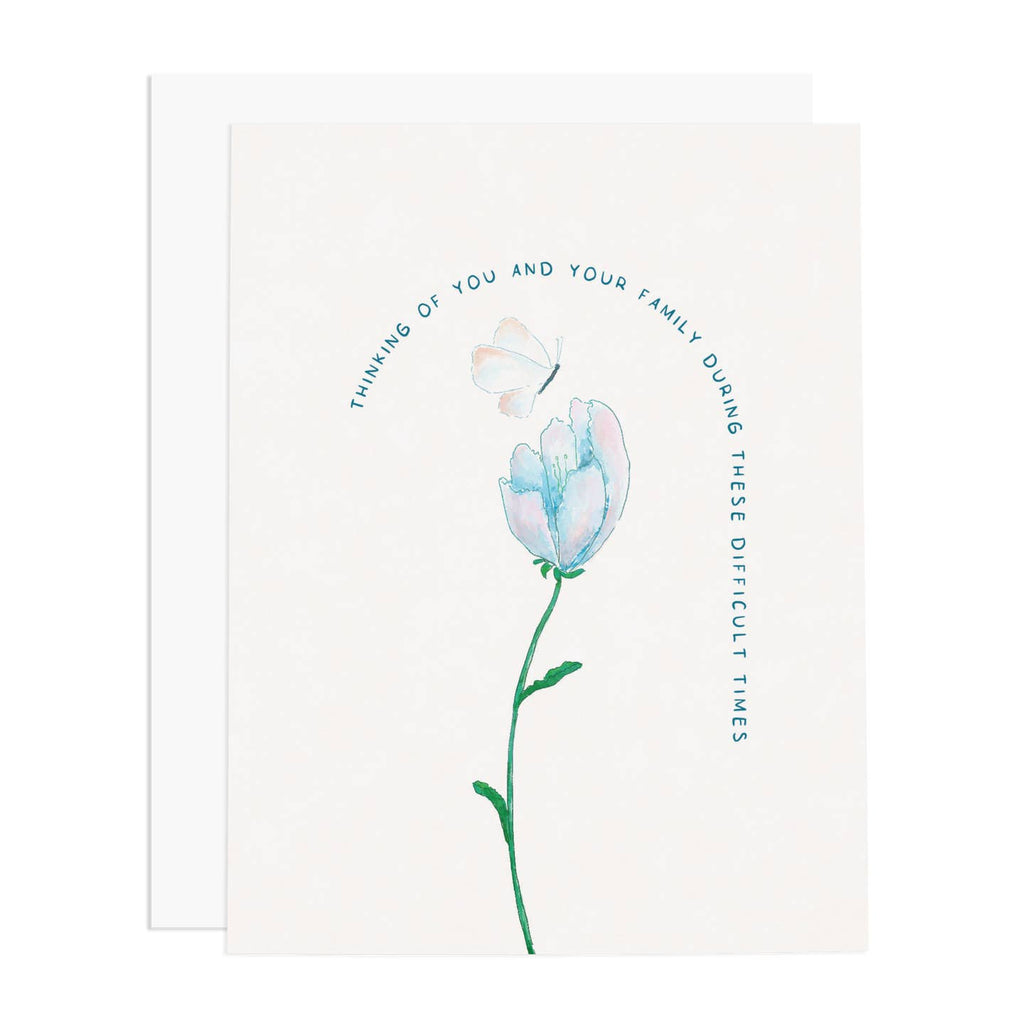 Greeting card with white background and image of a blue and pink flower with green stem and white butterfly and blue text says, "Thinking of you and your family during these difficult times." White envelope included. 