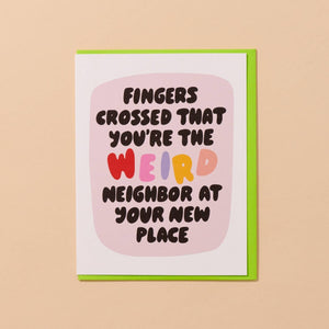 Greeting card with white background with pink center and black text says, "Fingers crossed that you're the weird neighbor at your new place". Neon green envelope included. 