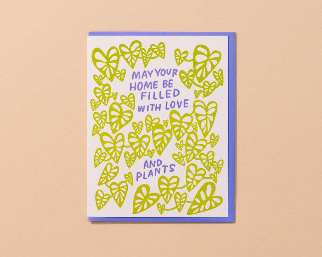 Greeting card with white background and images of neon green plant leaves and lilac text says, "May your home be filled with love and plants". Lilac envelope included. 