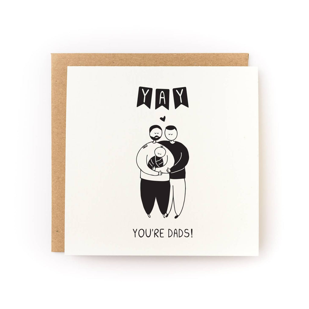 Greeting card with cream background and image of two men holding a baby, Black text says, "Yay You're Dads!". Kraft envelope included.
