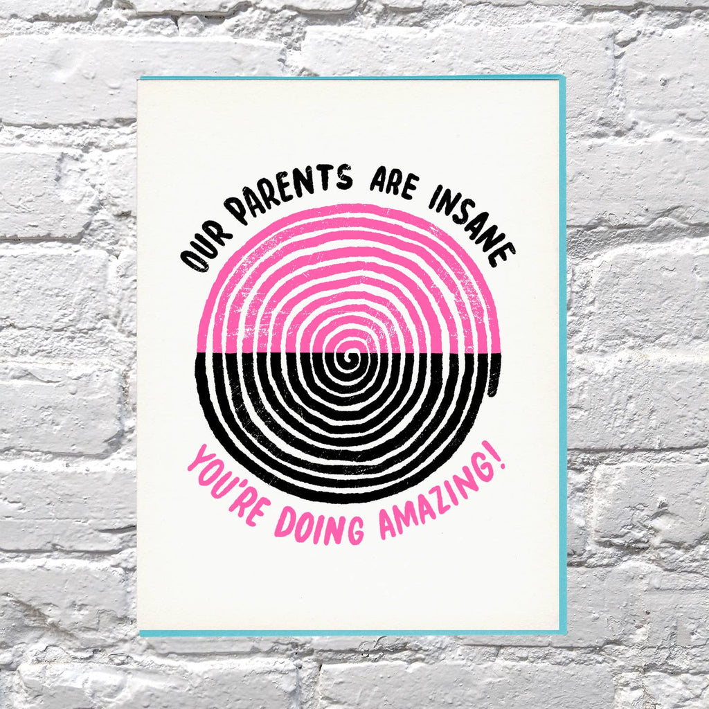 Greeting card with white background with a pink and black spiral in the middle with black text says, "Our parents are insane" and pink text says, "You're doing amazing!".  Teal envelope included. 