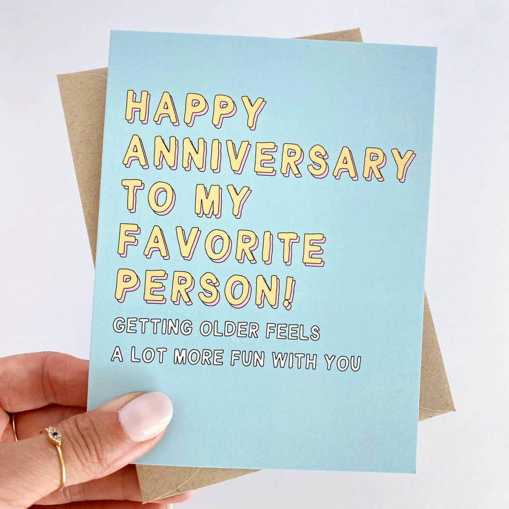 Blue card with yellow lettering that says "Happy anniversary to my favorite person!" White text underneath says "Getting older feels a lot more fun with you"