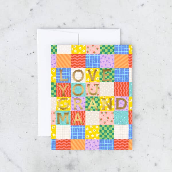 Greeting card with colorful patchwork quilt background with gold foil text says, "Love you Grandma". White envelope included.