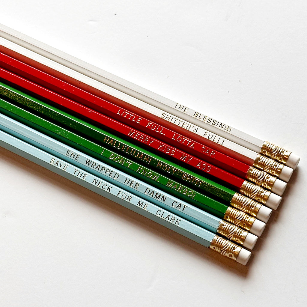Eight pencils with gold foil text says, "Merry Kiss My Ass Little Full. Lotta Sap. The Blessing! Shitter's Full! Hallelujah! Holy Shit! I Don't Know, Margo! She Wrapped Her Damn Cat Save The Neck For Me, Clark. 