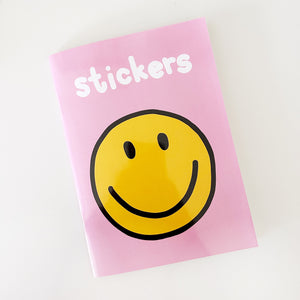 Image of sticker book with pink background and images of yellow smiley face and white puffy text says, "Stickers". 