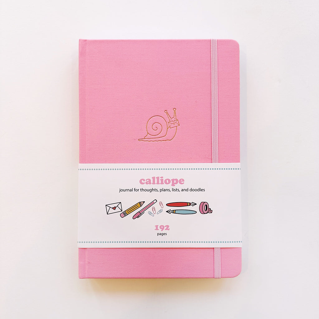 Image of pink journal with image of gold foil snail and pink elastic strap on right side to hold closed. 