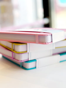 Image of stack of journals in pink, chartreuse, lilac and teal. 