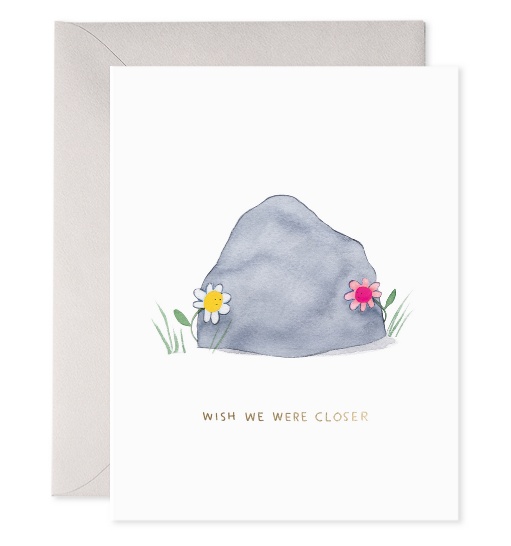 White background with image of a grey boulder with a white daisy and a pink daisy on opposite sides. Grey text says, "Wish we were closer". Silver envelope included.