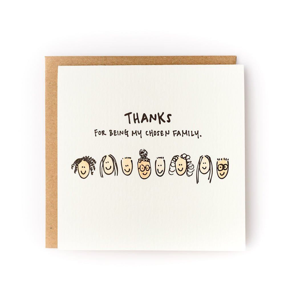 Square white card with black text saying, "Thanks For Being My Chosen Family". Images of several types of people's faces across center of card. A brown envelope is included.