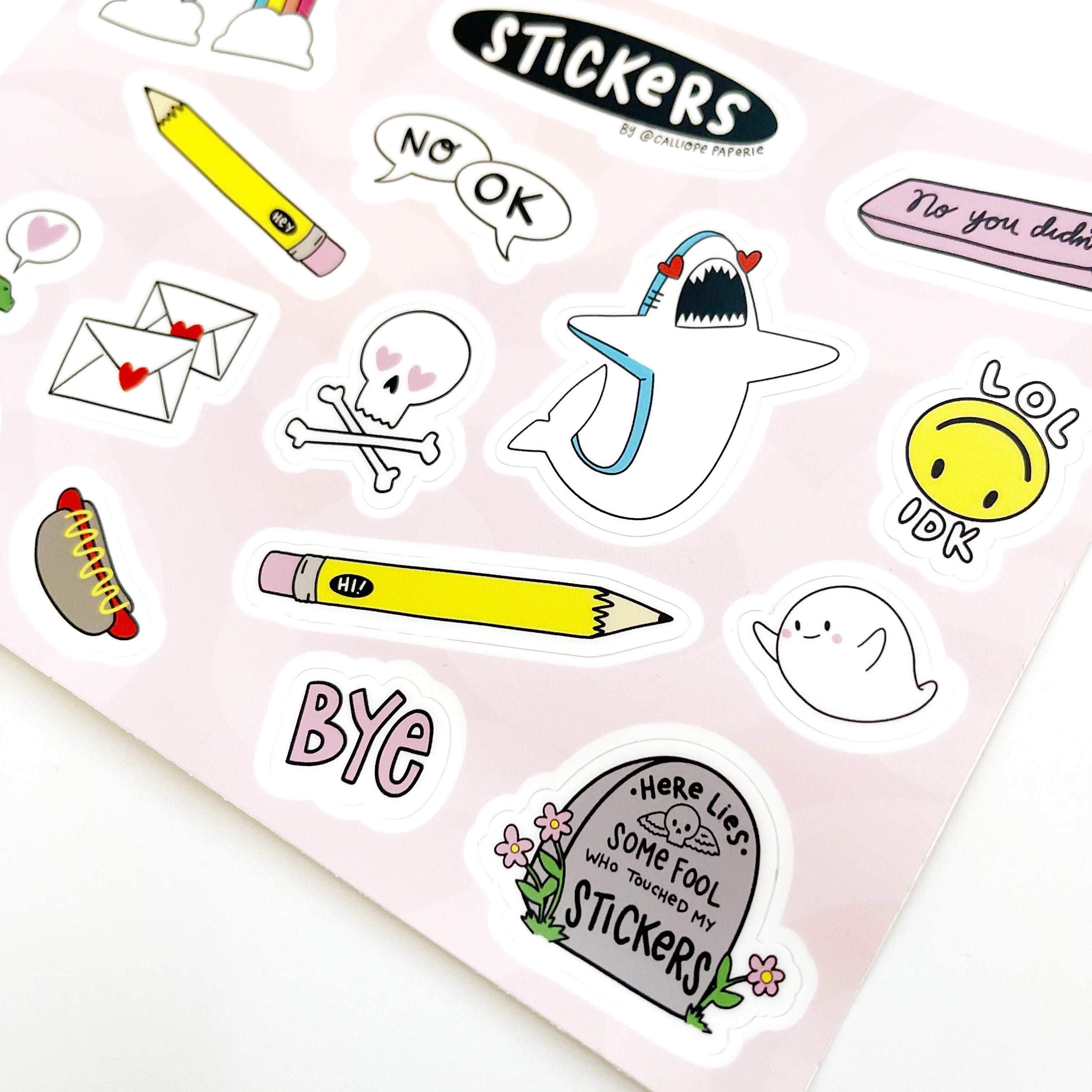 Pink background with sticker images of green dinosaur, yellow pencil, rainbow with clouds, shark, ghost, and pink eraser.