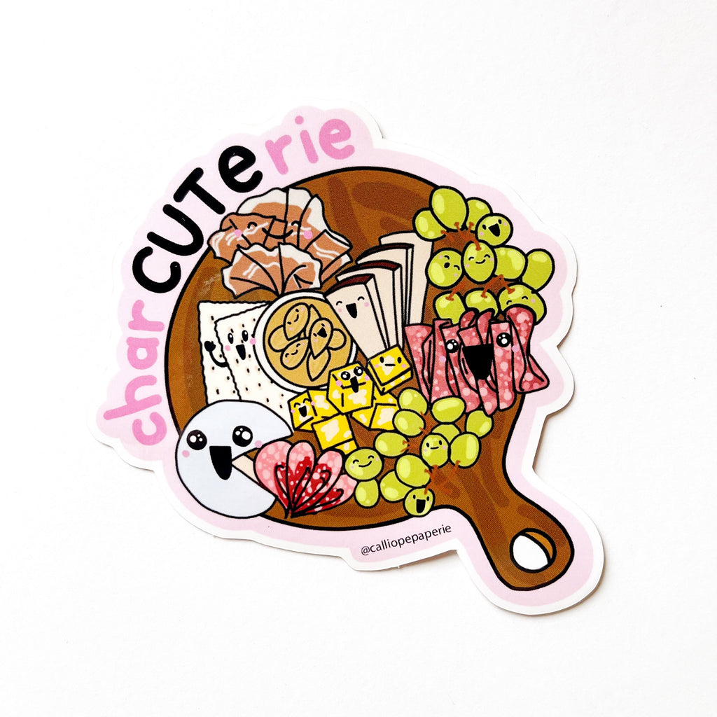 A charcuterie board with different meats, cheese, and fruits. Each element of food has a cute face. Everything sits on a round cheeseboard with a handle. Text around the outside says "char CUTE rie"