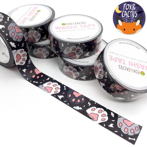 Decorative tape with black background with images of gray, black and white paw prints. 