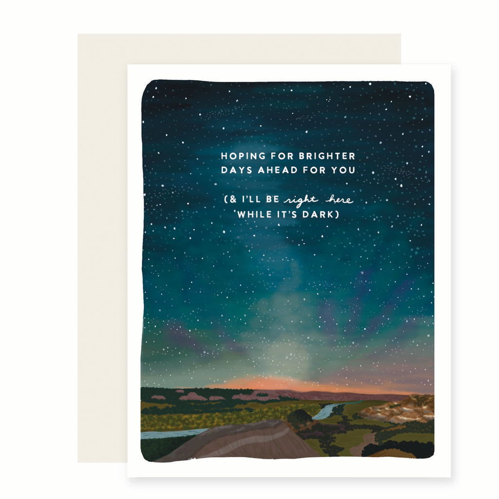 White card with image of a scenic river flowing into the mountains with a blue and green night sky above with white stars. White text saying, “Hoping for Brighter Days Ahead For You (& I’ll Be Right Here While It’s Dark)”. An ivory envelope is included.