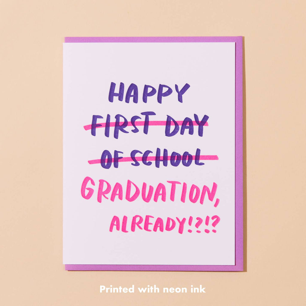 White card with dark purple text saying “Happy First Day of School” with “first day of school” crossed out in bright pink lines followed by text saying "Graduation already!?1?”. Light purple envelope included. 