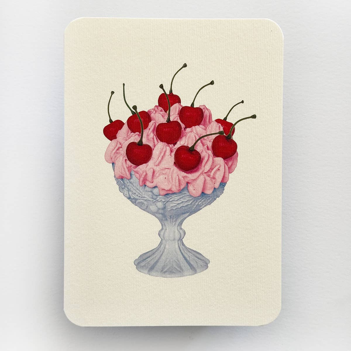 Greeting card with cream background and image of pink Chantilly cream dessert covered in stemmed cherries in a white footed dish. Envelope included.