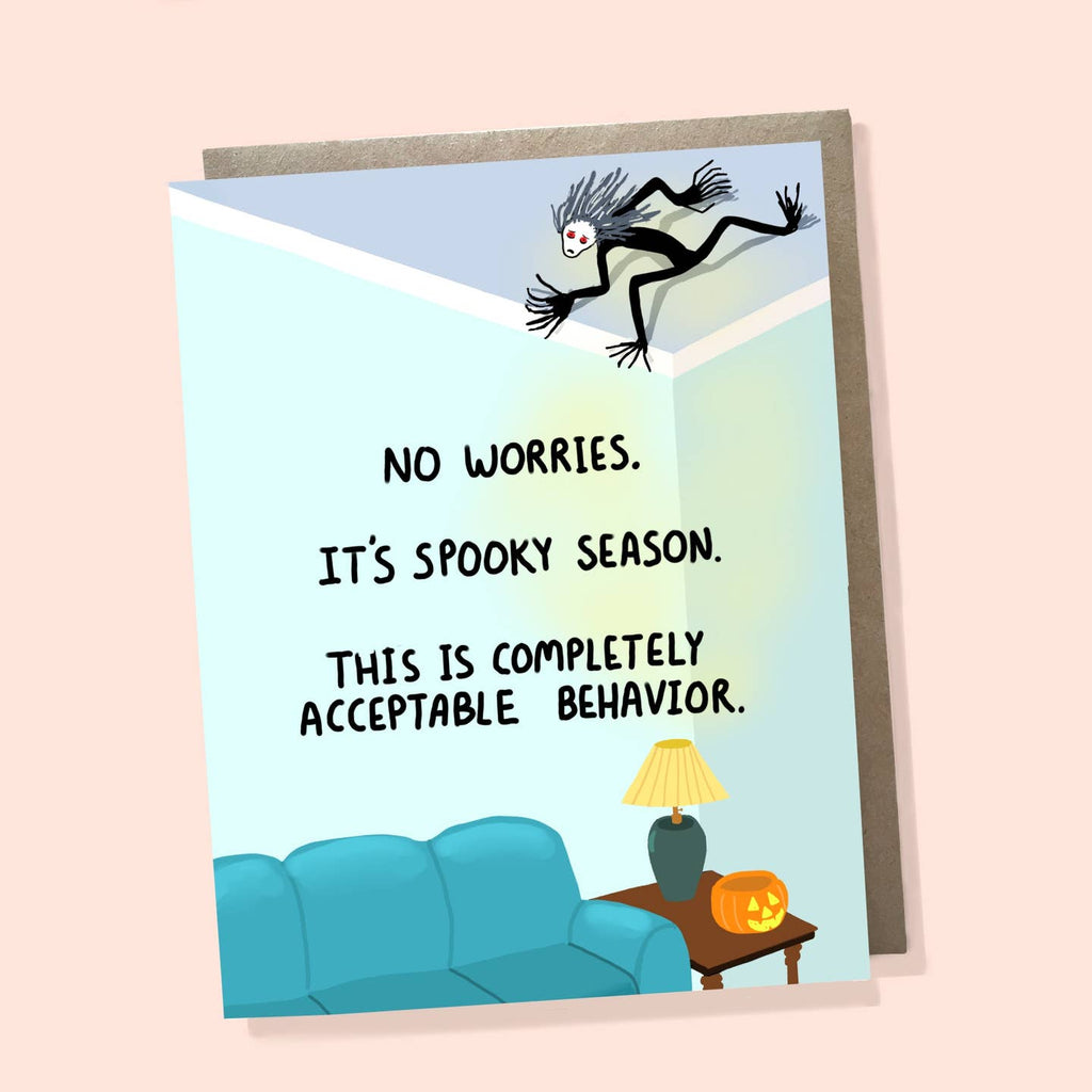 Greeting card with blue background with image of a teal couch with end table and lamp with pumpkin. Black spider person on the ceiling. Black text says, "No worries. It's spooky season. This is completely acceptable behavior." Kraft envelope included. 