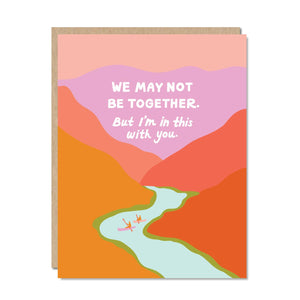 Pink sky with image of river in pale blue with image of tow people in canoes. White text says, “We may not be together. But I’m in this with you.” Kraft envelope included.   