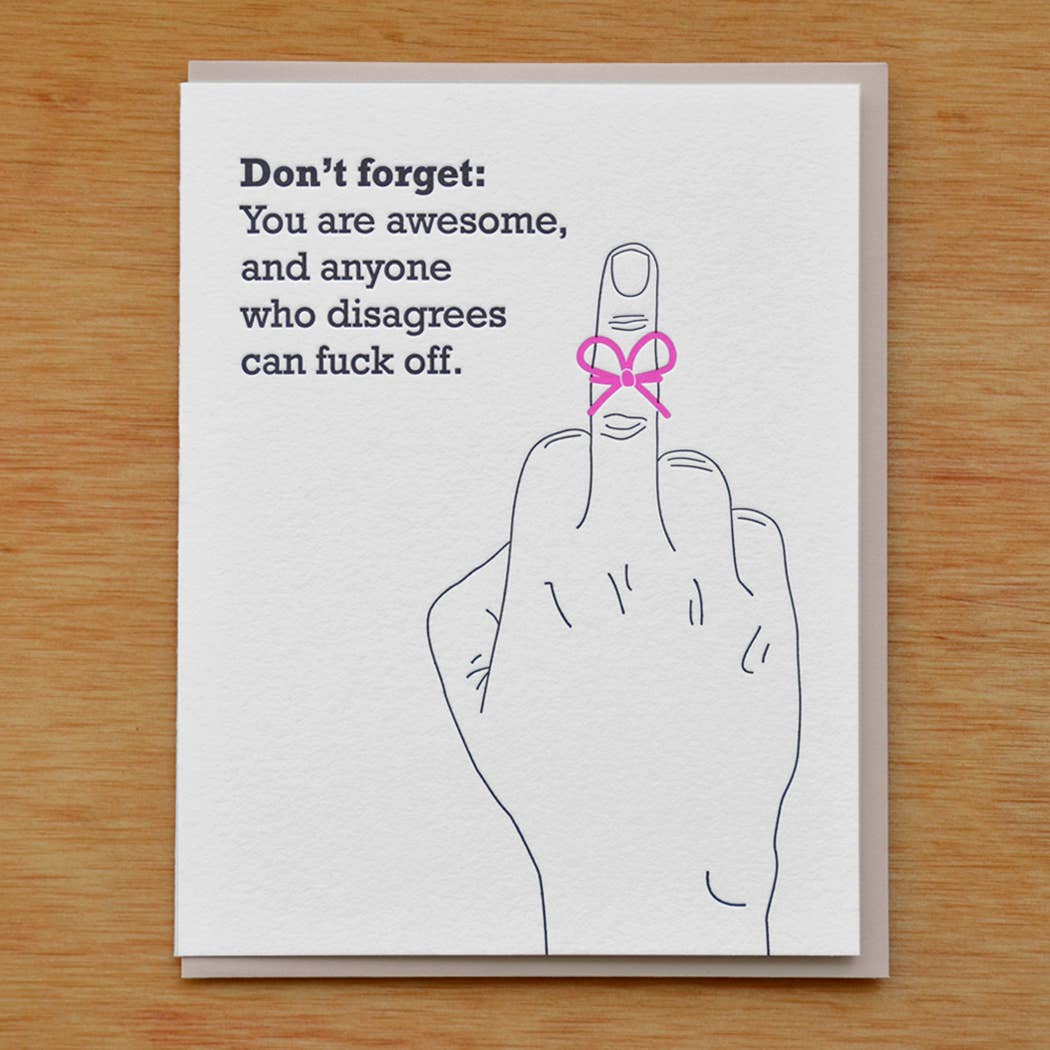 Greeting card with white background and image of a hand with a middle finger raised and tied with a pink bow. Black text says, "Don't forget: You are awesome, and anyone who disagrees can fuck off." Tan envelope included.