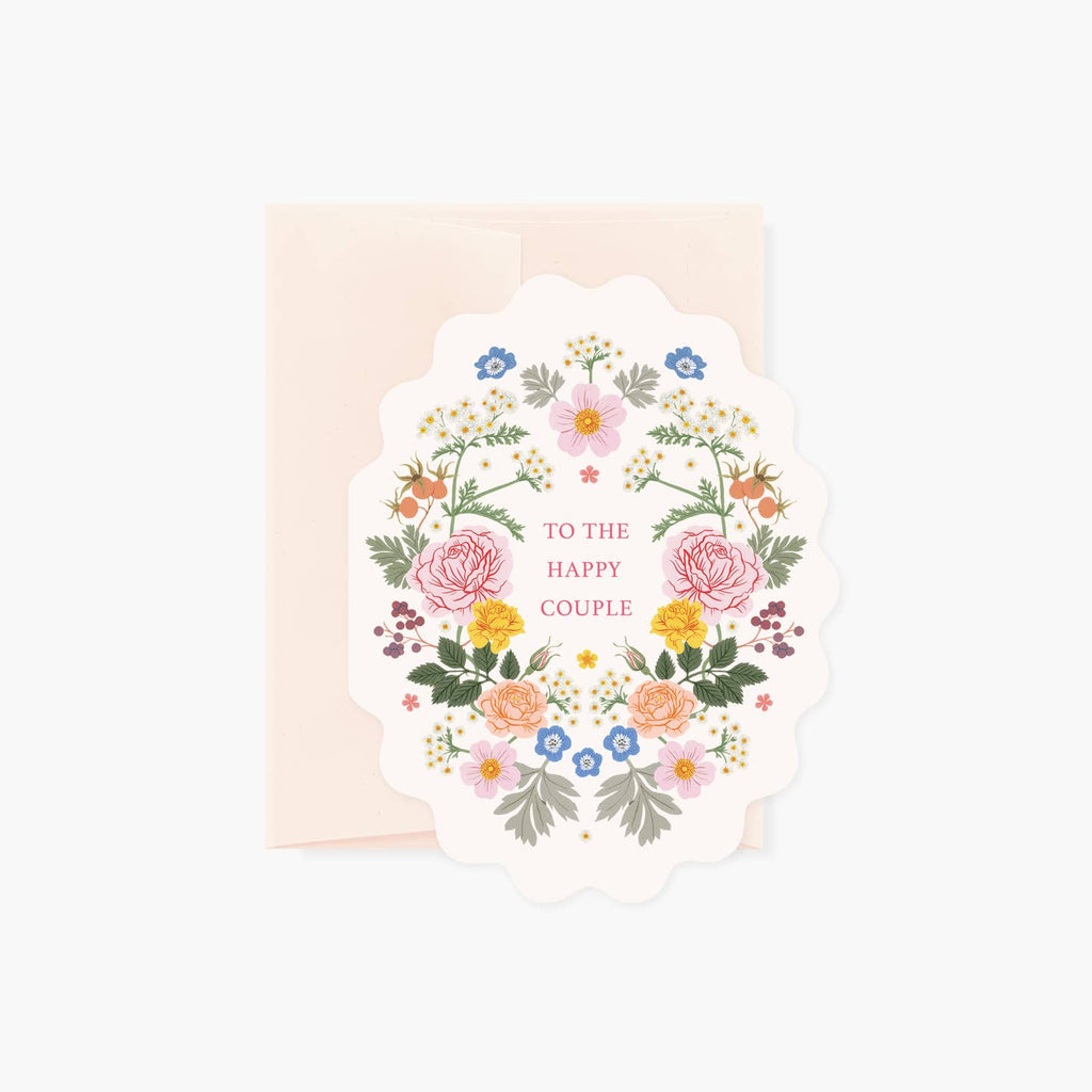 Oval scalloped ivory background with pink, yellow, red and orange flowers with green leaves and stems. Pink text says, “To the happy couple” in the center. Pale pink envelope is included.       