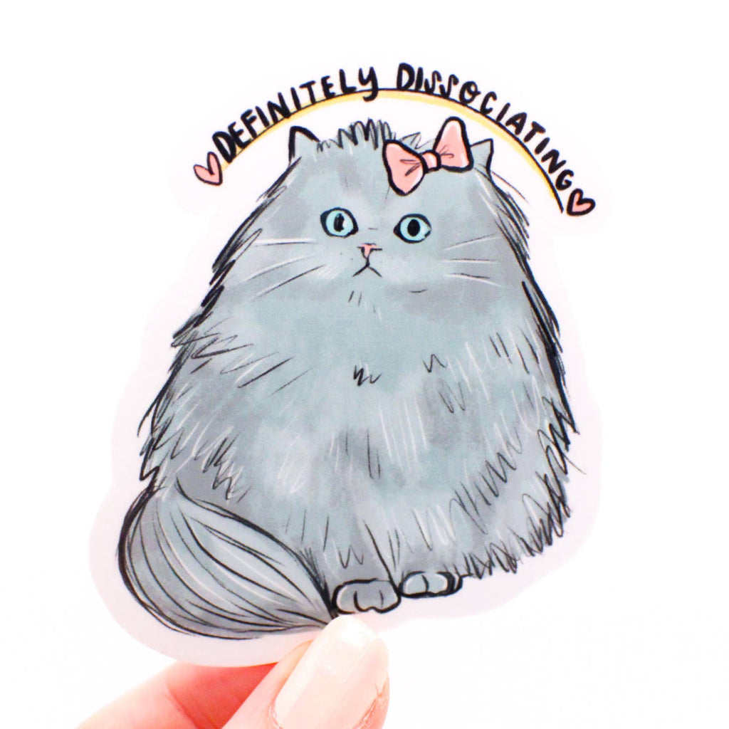 Image of grey fluffy kitty with blue eyes and a pink bow with black text says, "Definitely dissociating". 