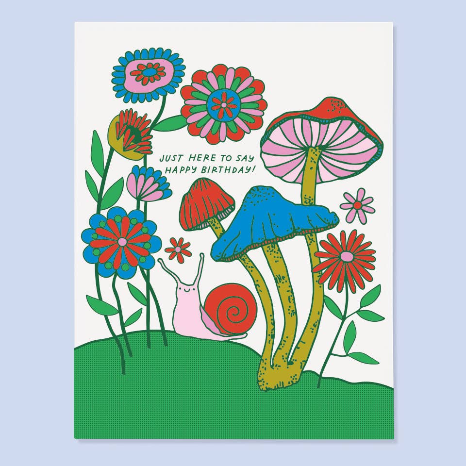 White background with images of flowers and mushrooms with a pink and red snail, Green text says, "Just here to say happy birthday!". Envelope included.