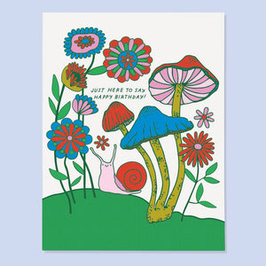 White background with images of flowers and mushrooms with a pink and red snail, Green text says, "Just here to say happy birthday!". Envelope included.