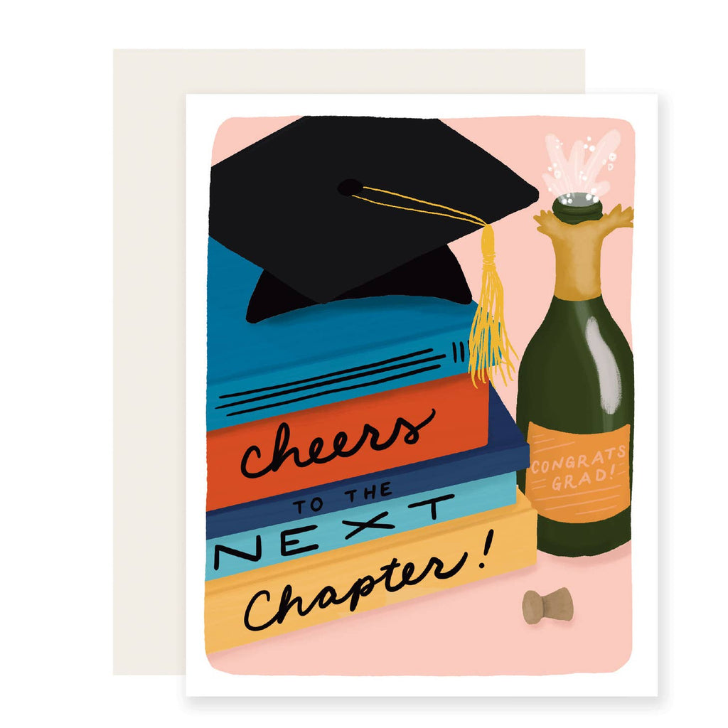 Greeting card with pink background and image of stack of books and graduation cap and a bottle of champagne. Black text on book bindings say, "Cheers to the next chapter!". Cream envelope included.