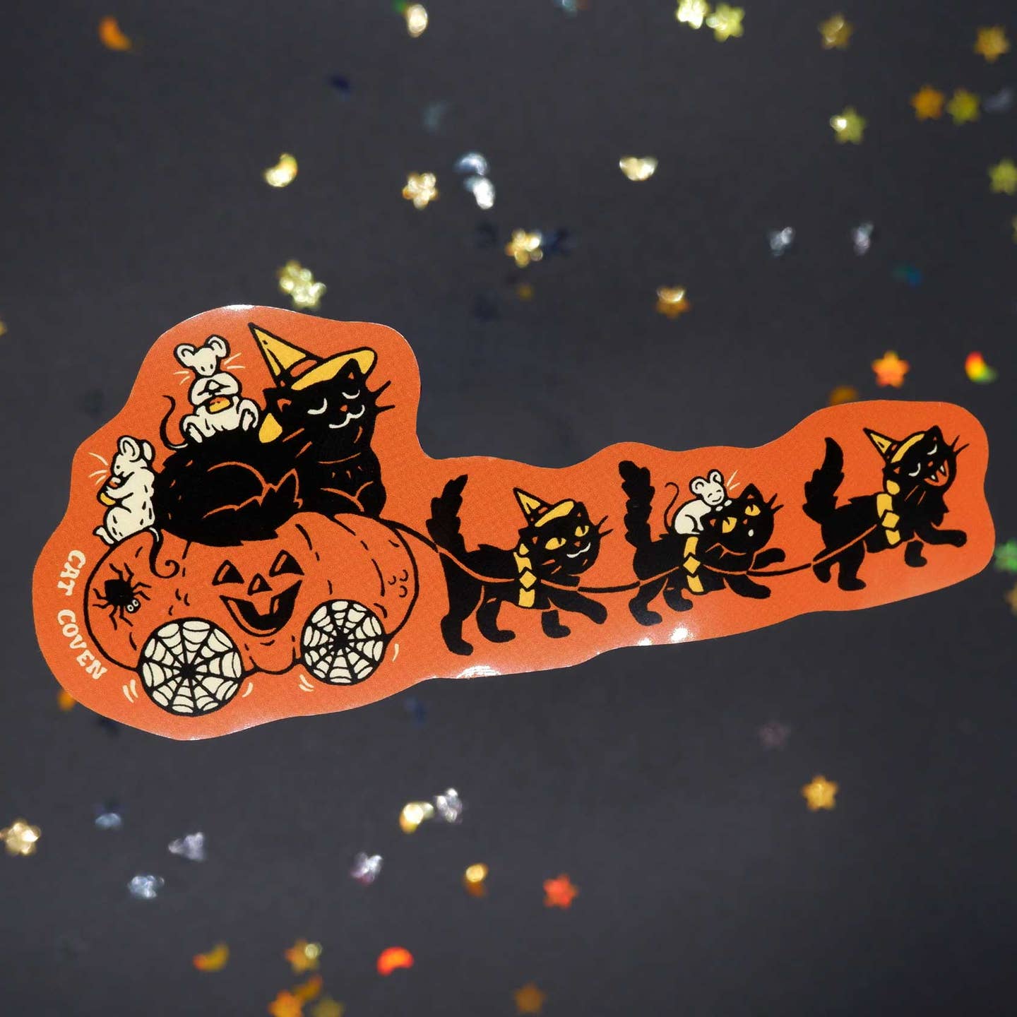 Decorative sticker with orange background and image of a pumpkin carriage with black cats riding and pulling the carriage.
