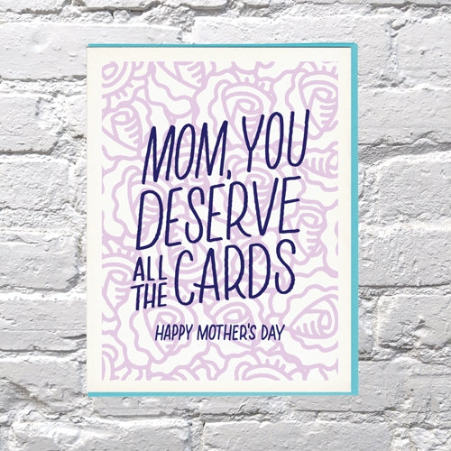 Greeting card with white background  with images of lilac outlined flowers with blue text says, "Mom, You deserve all the cards, Happy Mother's Day". Teal envelope included. 