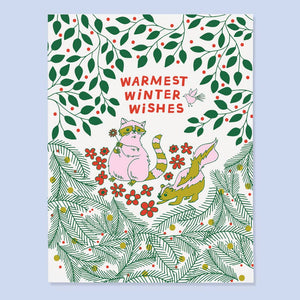 Greeting card with white background and pine branches on bottom of card and green vines with red berries on top of card. Image of a pink raccoon holding a flower and a skunk with red text says, "Warmest winter wishes". Envelope included.