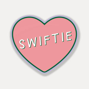 Decorative sticker  in heart shape with pink background and white text says, "Swiftie". 