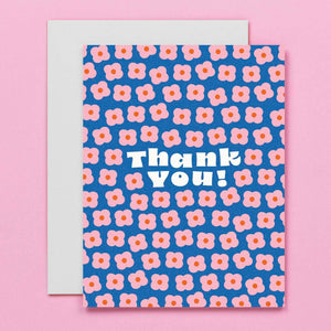 Greeting card with blue background with images of small pink flowers with red centers and white text says, "Thank you!". Envelope included.