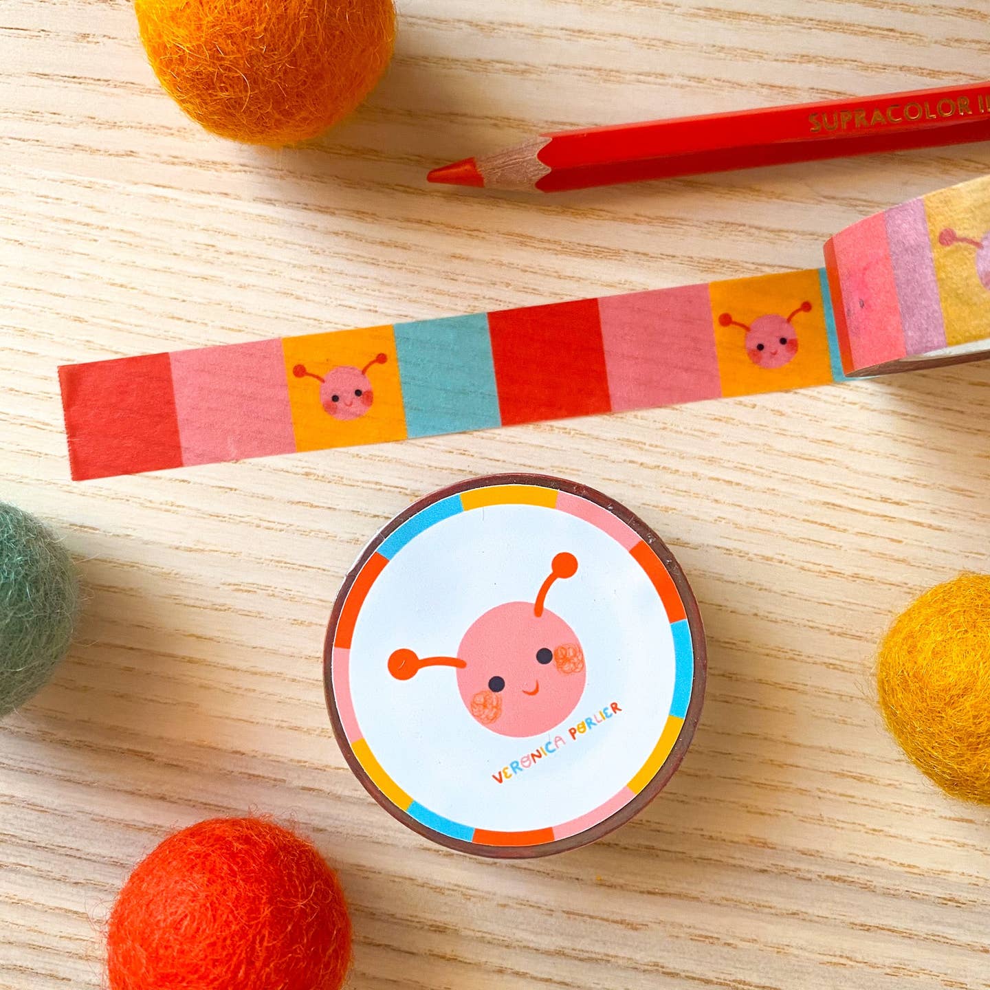 Decorative tape with color block background in red, pink, yellow and aqua with image of caterpillar face in pink and orange. 