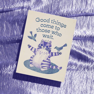 Greeting card with cream background and blue image of a striped cat with its arms stretched out and two bird landing on its arms. Blue text says, "Good things come to those who wait.". Envelope inclosed.