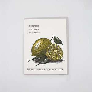 Greeting card with white background and image of lemons with grey text says, "THis sucks, they suck, that sucks, Sorry everything sucks right now". Grey envelope included.