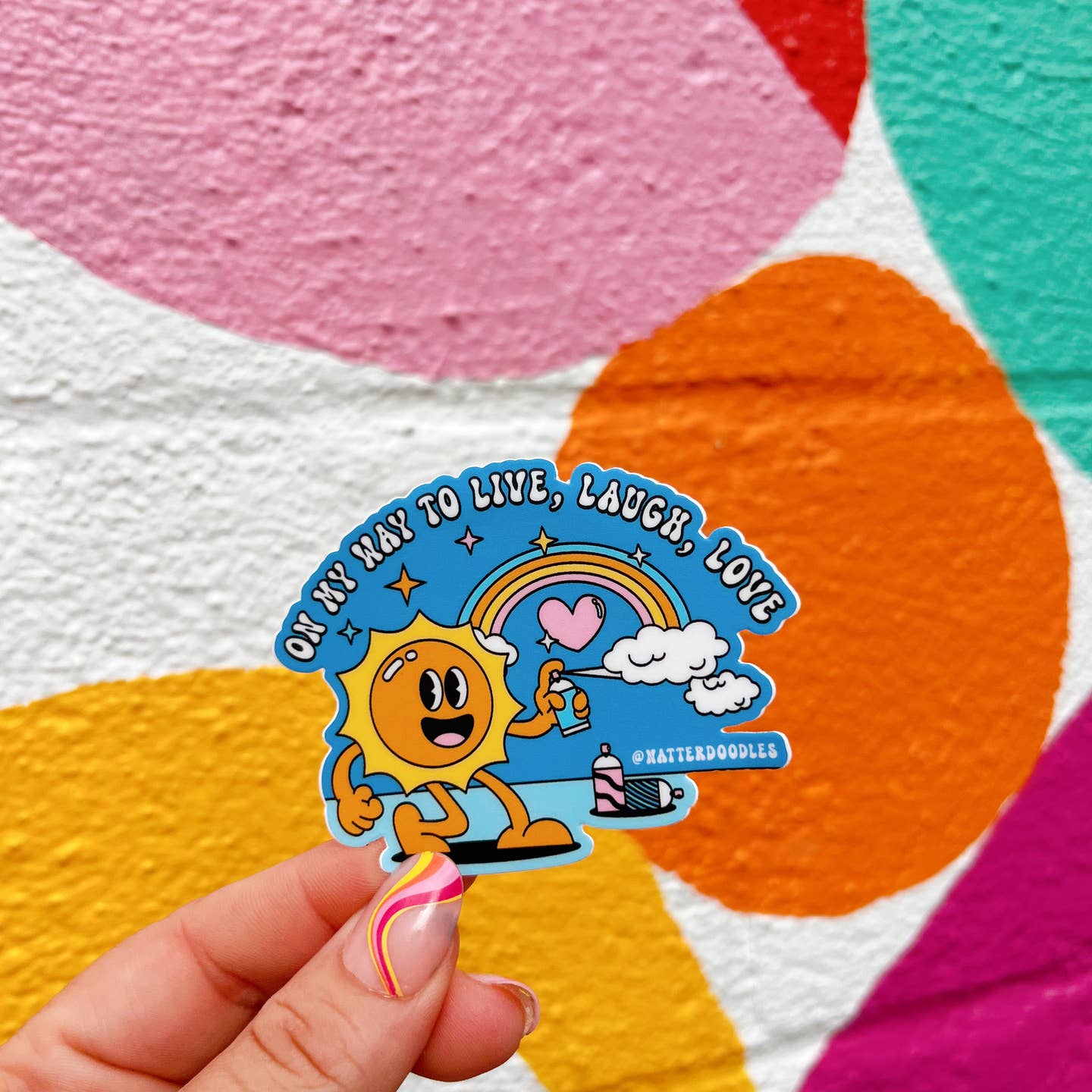 Decorative sticker with blue background and image of a sun, rainbow and spray can making clouds. White text says, "On my way to live, laugh, love". 