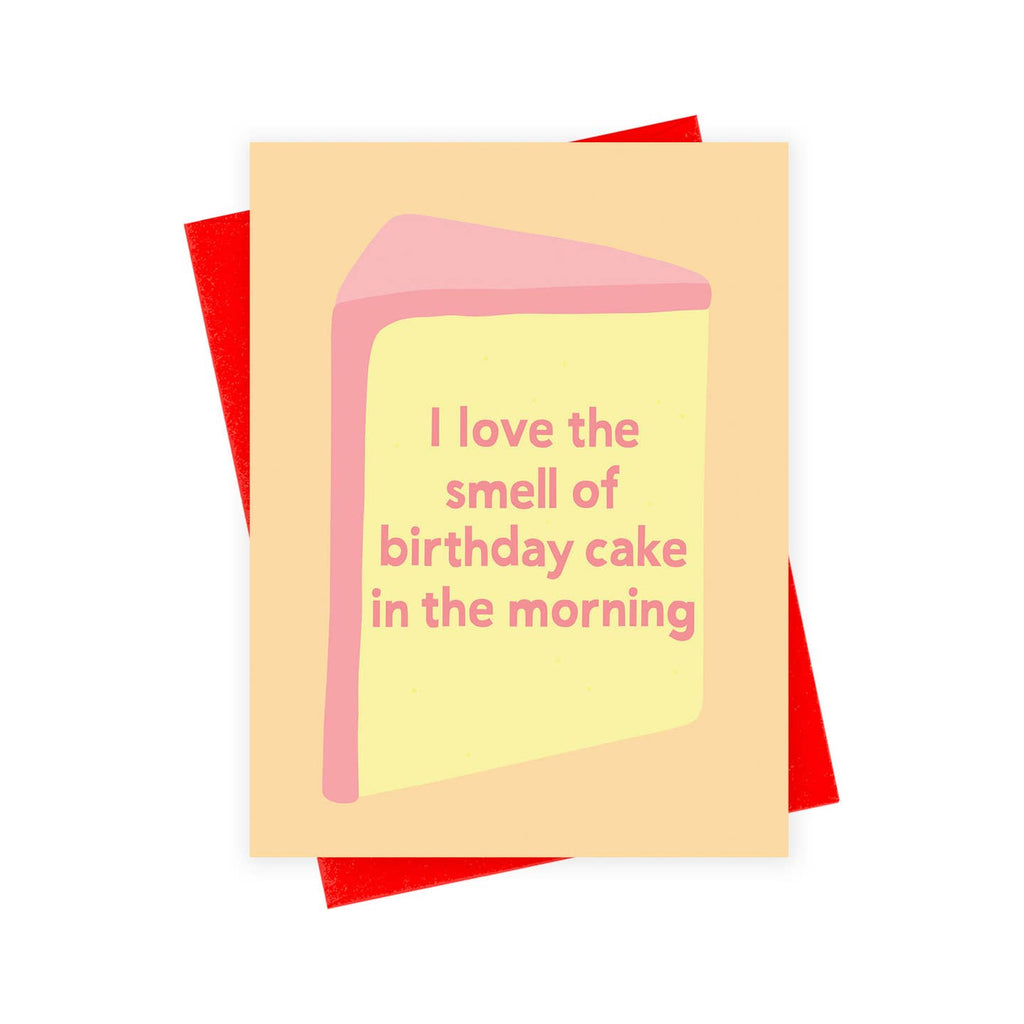 Greeting card with peach background and image of a piece of cake in yellow with pink frosting. Pink text says, "I love the smell of birthday cake in the morning". Red envelope included. 