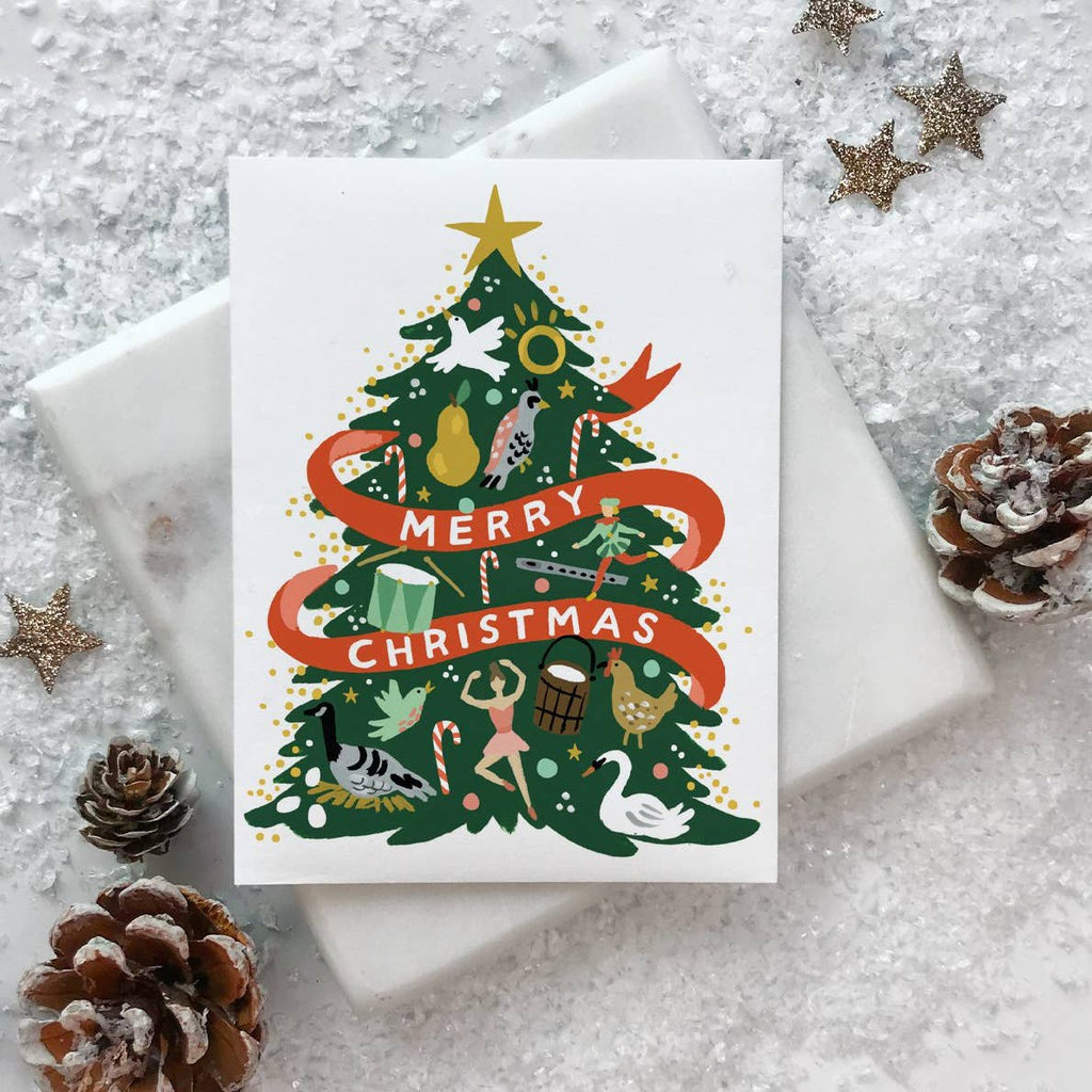 Greeting card with white background and image of a green Christmas tree with a red banner with white text says, "Merry Christmas" and images of twelve days of Christimas items. White envelope included. 