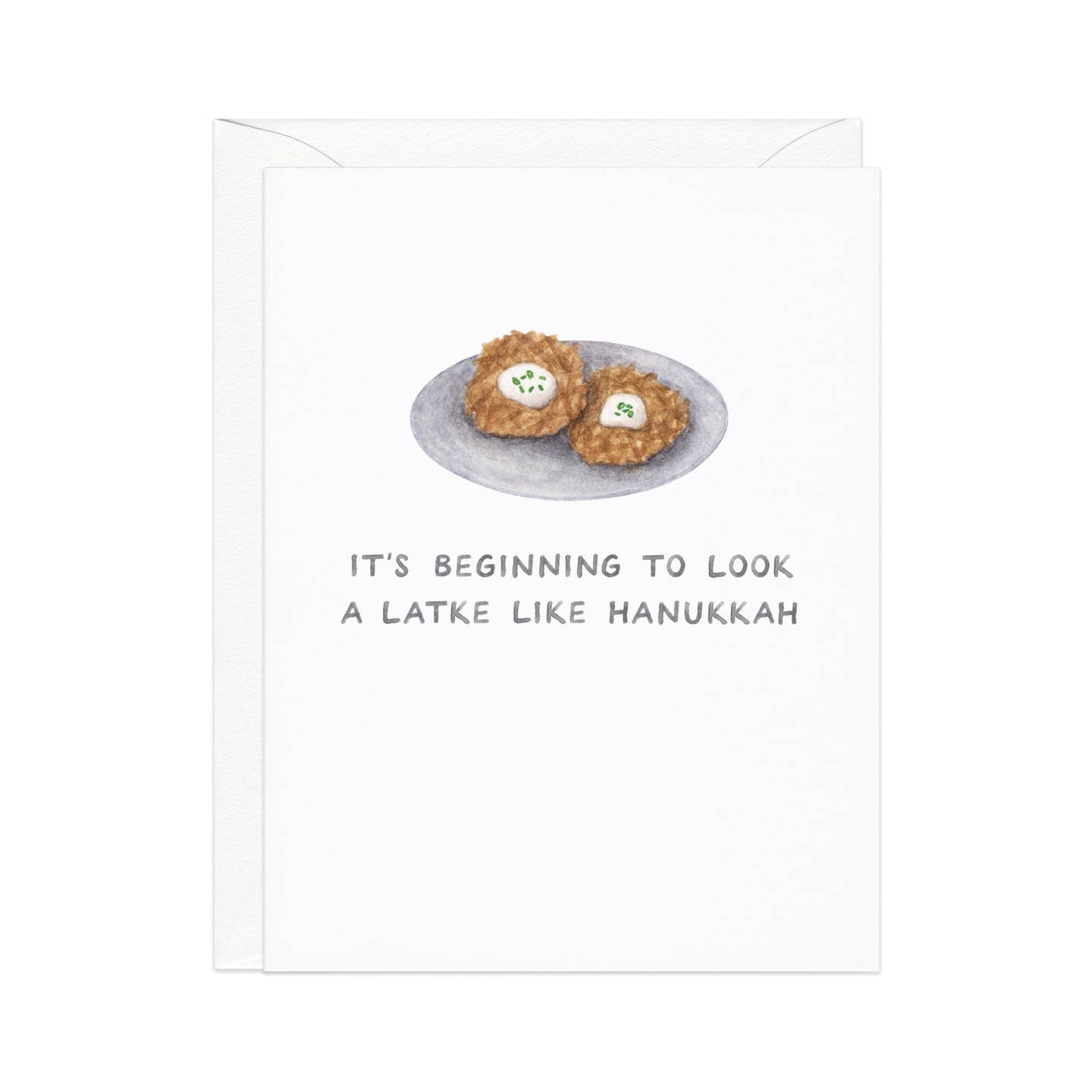 Greeting card with white background and image of a plate of latkes with grey text says, "It's beginning to look a latke like Hanukkah". White envelope included. 