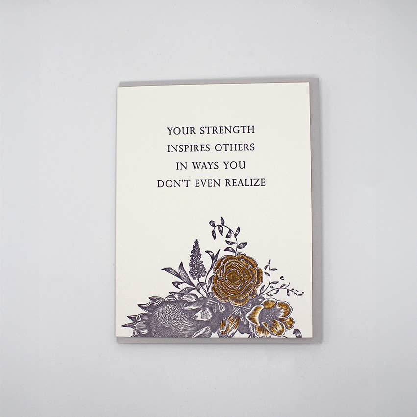 Greeting card with image of bouquet of flowers at bottom of card and black text says, "Your strength inspires others in ways you don't even realize". Grey envelope included.