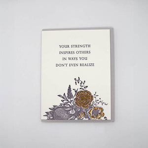 Greeting card with image of bouquet of flowers at bottom of card and black text says, "Your strength inspires others in ways you don't even realize". Grey envelope included.