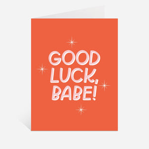 Greeting card with dark apricot background and pink and white text says, "Good luck, Babe!". Envelope included. 