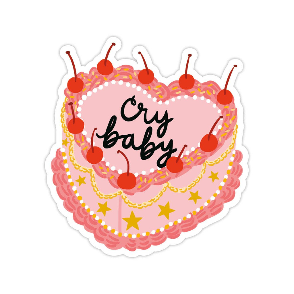 Image of a pink and red heart shaped cake with cherries and gold stars and black text says, “Cry baby”.   