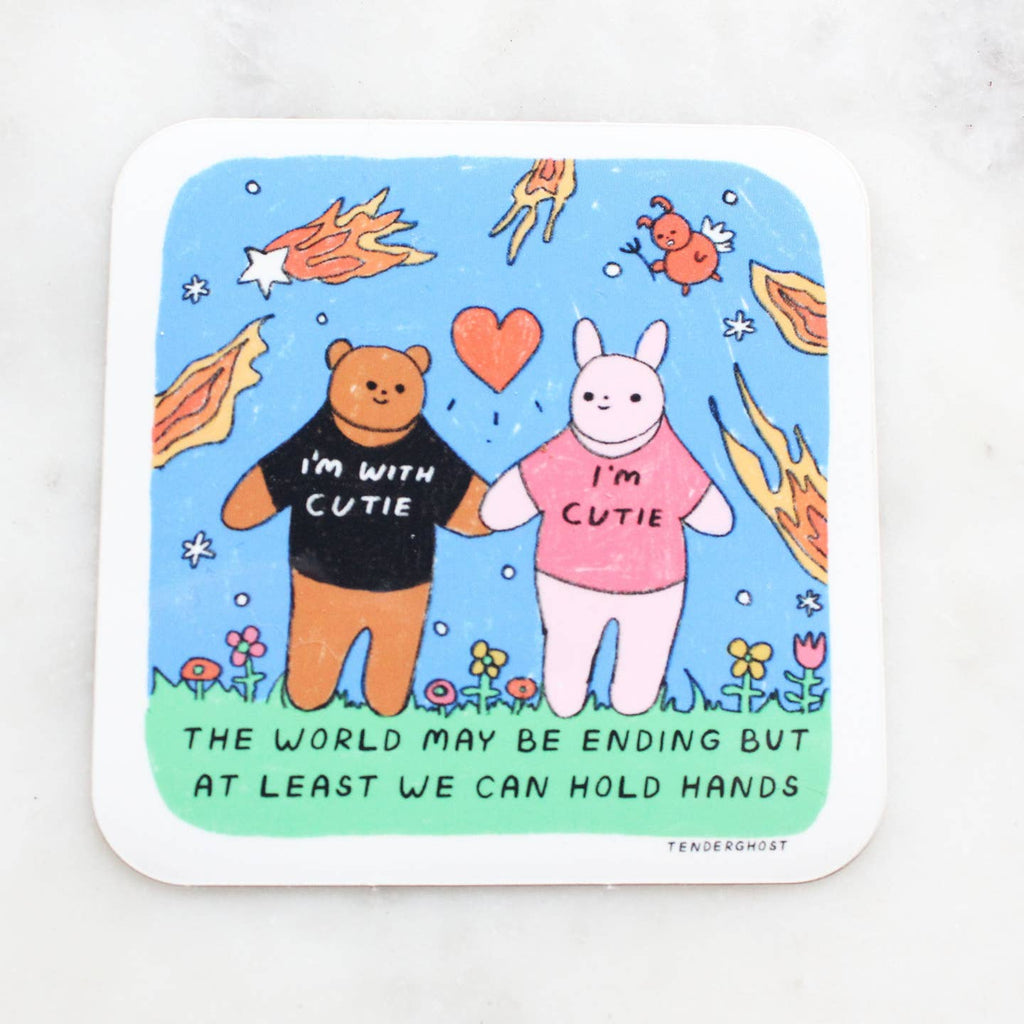 Sticker with blue and green background with image of a bear and a white bunny holding hands.  Bear has a shirt with "I'm with cutie" and bunny's shirt says, "I'm cutie". Fiery stars and a bird as a devil are around them. Black text says, "The world may be ending but at least we can hold hands". 