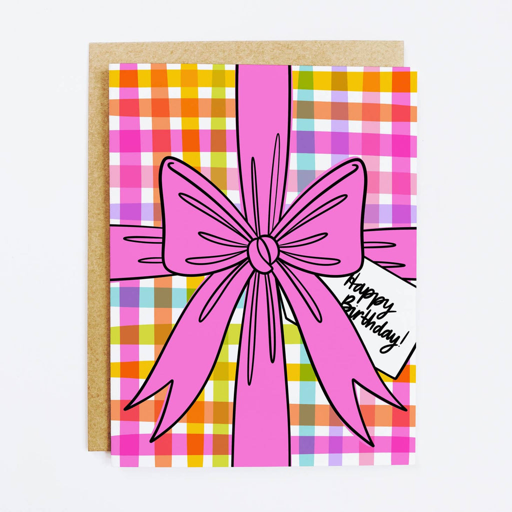Image of card with colorful plaid background with a pink bow and white gift tag with black text says, "Happy birthday". Kraft envelope included. 