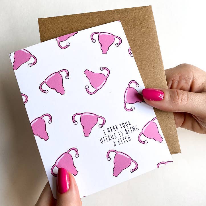 White card with a pattern of pink uterus shapes. Text says "I hear your uterus is being a bitch"