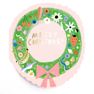 Greeting card in the shape of a holiday wreath in green with flowers, fruit and designs in white, black, red, pink, yellow and blue on a pink background. Envelope included. 