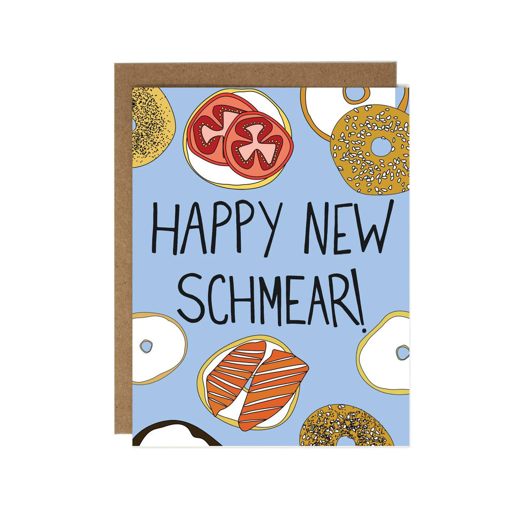 Greeting card with blue background with images of bagels and cream cheese with lox and tomatoes. Black text says, "Happy New Schmear!". Kraft envelope included. 